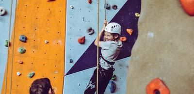 A child wearing a helment and harness holds onto a rope at Kendel climbing wall