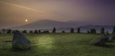 a moody sunrise casts light on stones at Castlerigg stone circle
