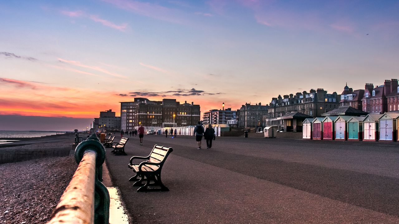 the seafront promenade of Brighton with colourful beach huts against a purple and orange sunset