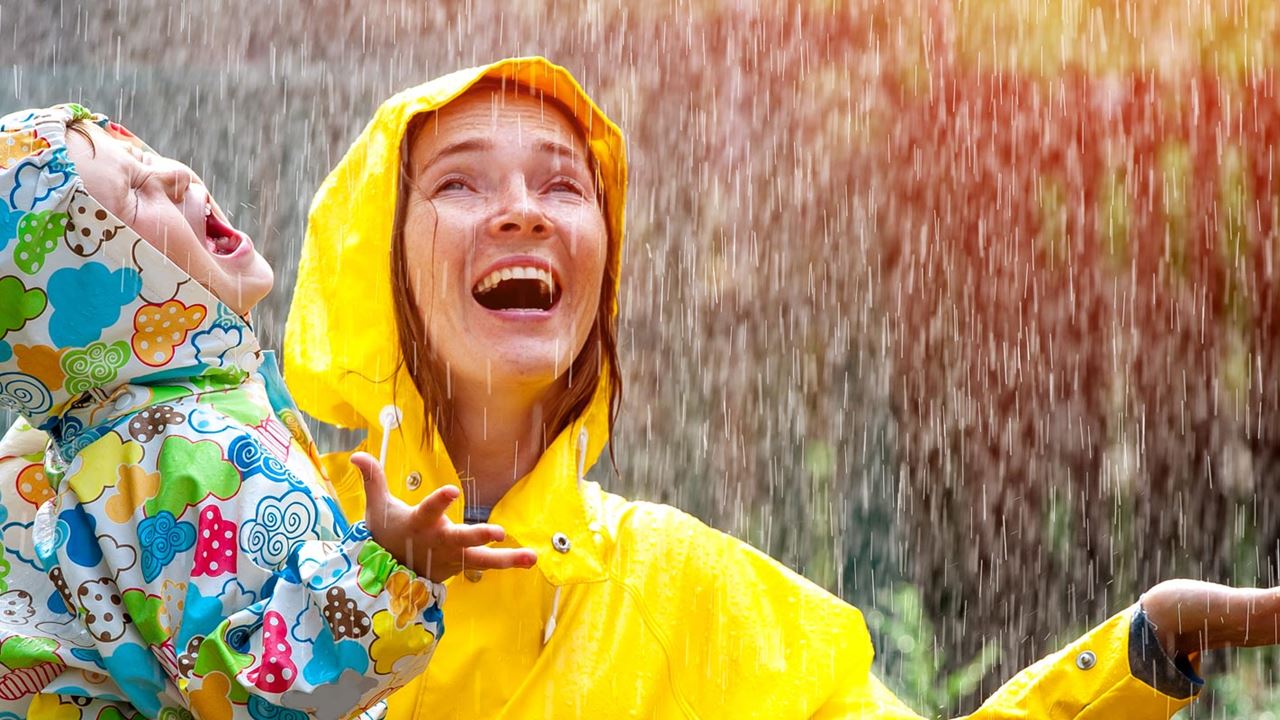Mother and daughter playing in the rain wearing colourful raincoats