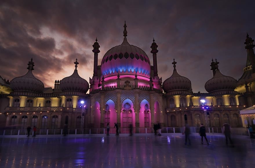 The Brighton Pavilion at night illuminated by pink and blue lights  with an ice skating rink and skaters 