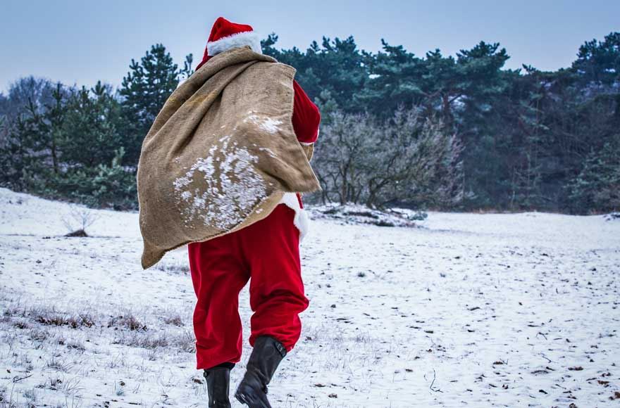 Santa walking through a snowy forest holding a sack on his back