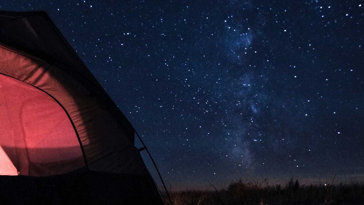 A red tent illuminated against a dark star filled sky