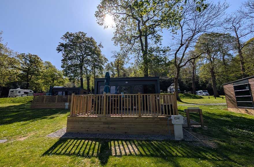 A glamping pod at Abbey Wood campsite, London. With the sun shining above the tall trees and blue sky