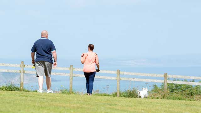 A man in shorts and a woman stroll along the cliff top by the sea