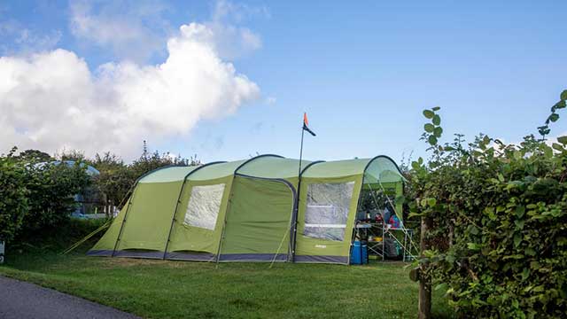 A large green tent with a flag is pitched against a blue sky