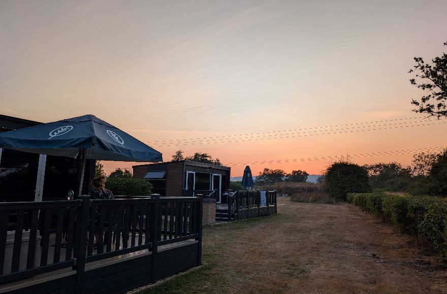 Row of glamping pods set along a grassy field looking out toward a vibrant orange sunset over the horizon.