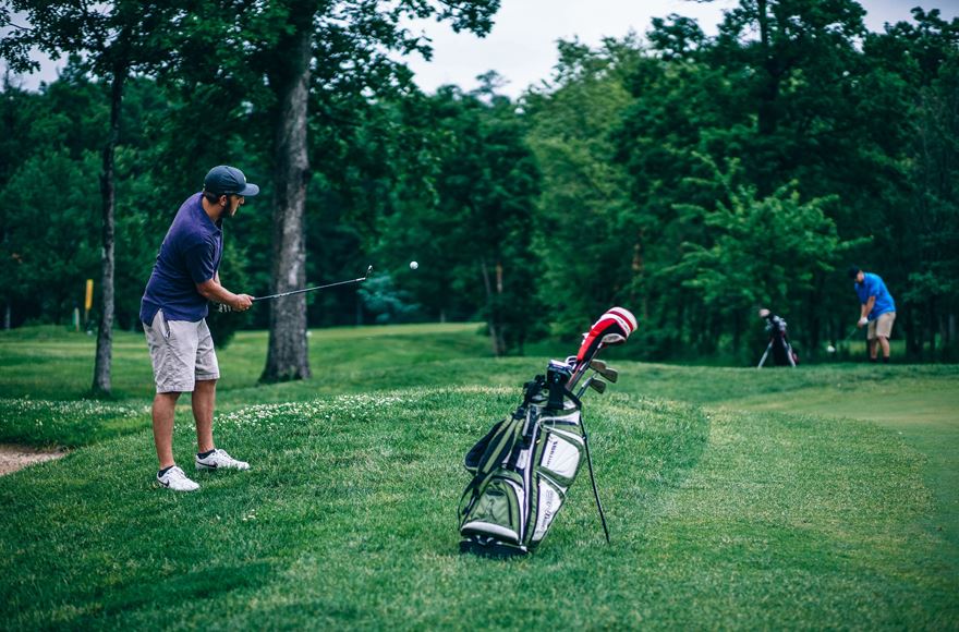 two men Playing golf on a pitch surrounded by trees 