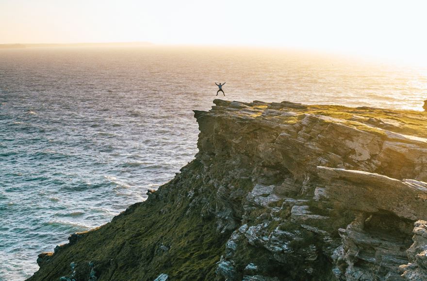  a man jumps in the air at the end of a large rocky cliff overlooking the sea 