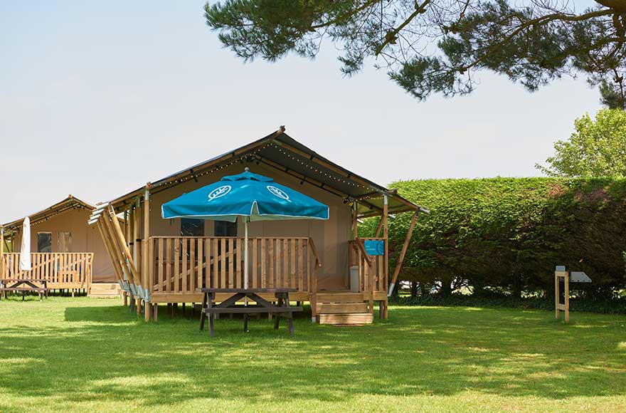 A grassy field with safari tent and umbrella on decking