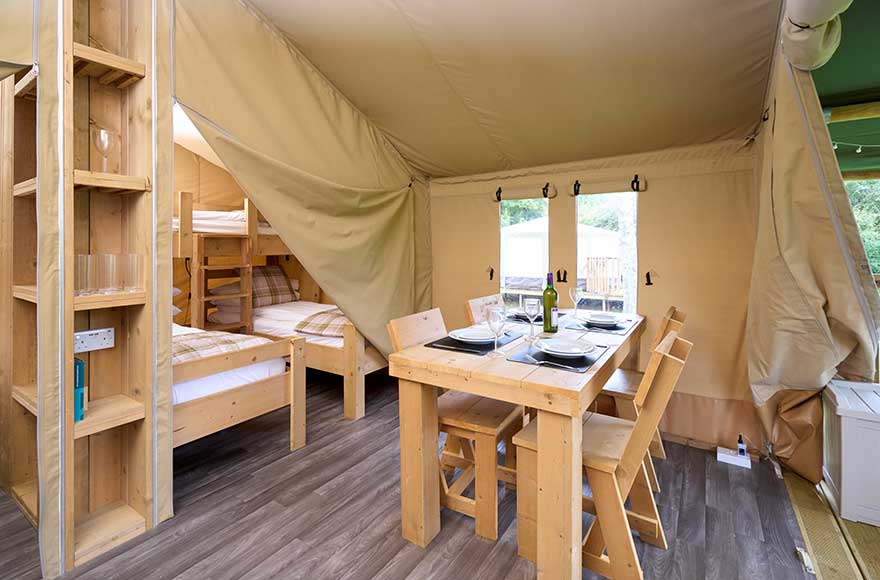 Inside the safari tent, a table and chairs are neatly set up, inviting guests to enjoy a meal in nature
