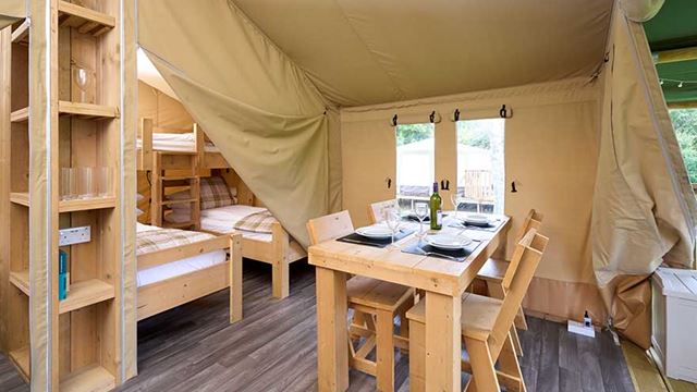 Inside the safari tent, a table and chairs are neatly set up, inviting guests to enjoy a meal in nature