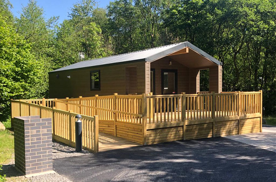 A cozy glamping cabin with a wooden wheelchair accessible deck and porch surrounded by trees