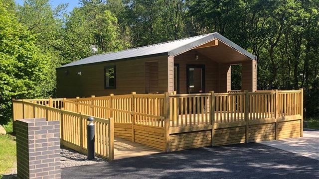 A cozy glamping cabin with a wooden wheelchair accessible deck and porch surrounded by trees