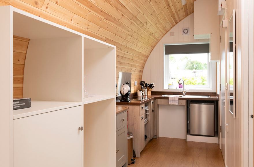 A compact kitchen featuring a sink, fridge and shelving 