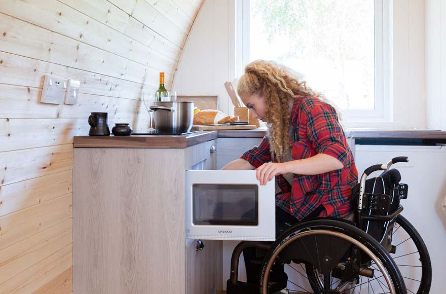 Woman in wheelchair opening microwave in kitchen area