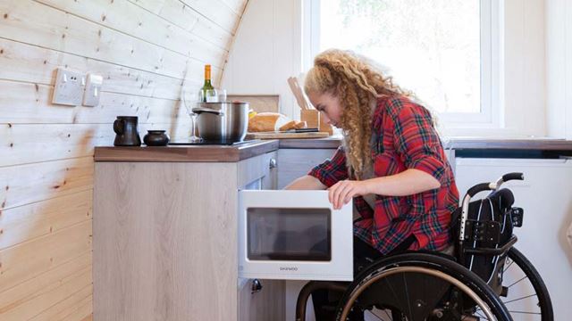 Woman in wheelchair opening microwave in kitchen area