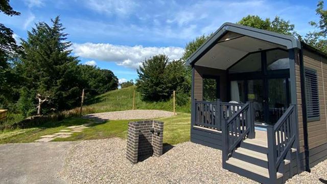 a glamping cabin with a bbq outside, located in a woodlands area