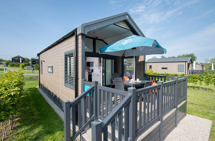 A cozy glamping cabin with a wooden deck and a table, surrounded by nature