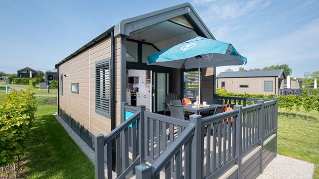 A cozy glamping cabin with a wooden deck and a table, surrounded by nature