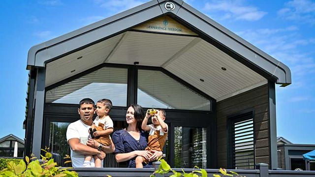 A happy family enjoying the outdoors, standing in front of their glamping cabin and a clear blue sky