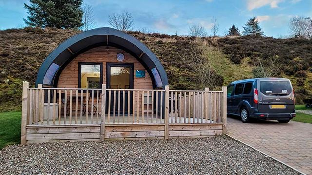 Exterior of glamping pod with lush green surroundings and a parking space