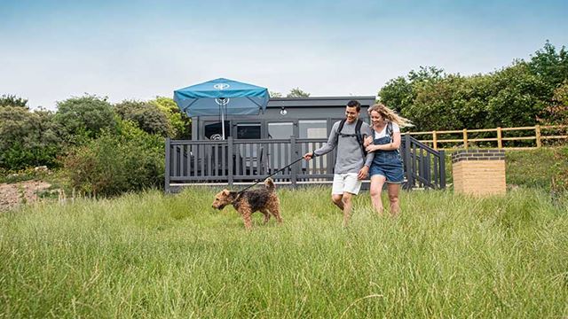 couple walking dog in long grass outside the glamping pod