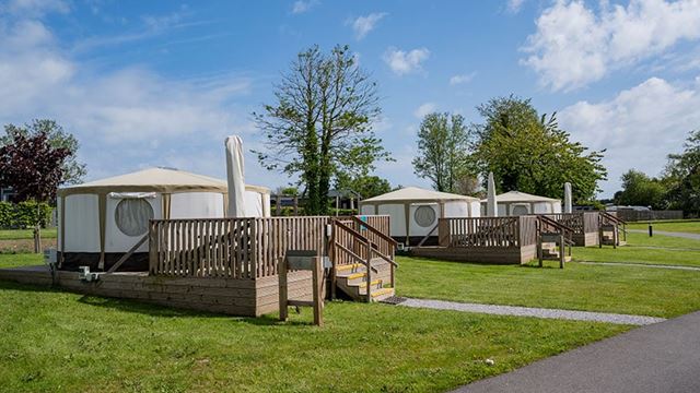 3 canvas yurts with outdoor decking surrounded by grass on a backdrop of trees