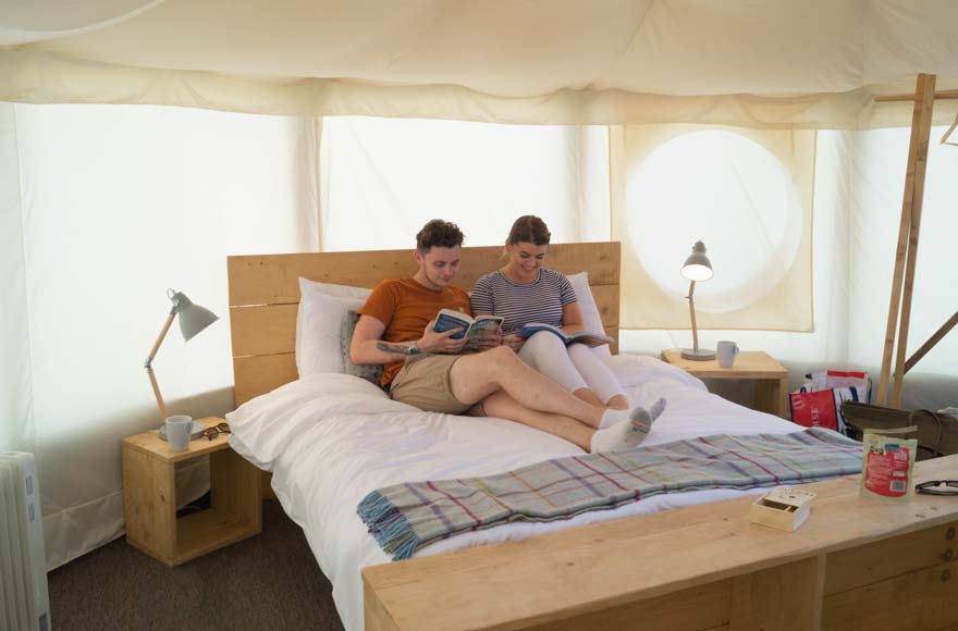 A couple relaxing on a bed inside a canvas yurt