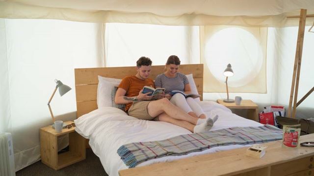 A couple relaxing on a bed inside a canvas yurt