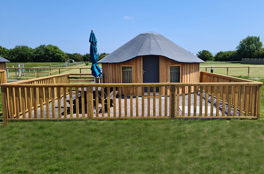 wooden yurt enclosed by a wooden fence in an open field