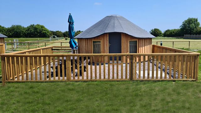 wooden yurt enclosed by a wooden fence in an open field