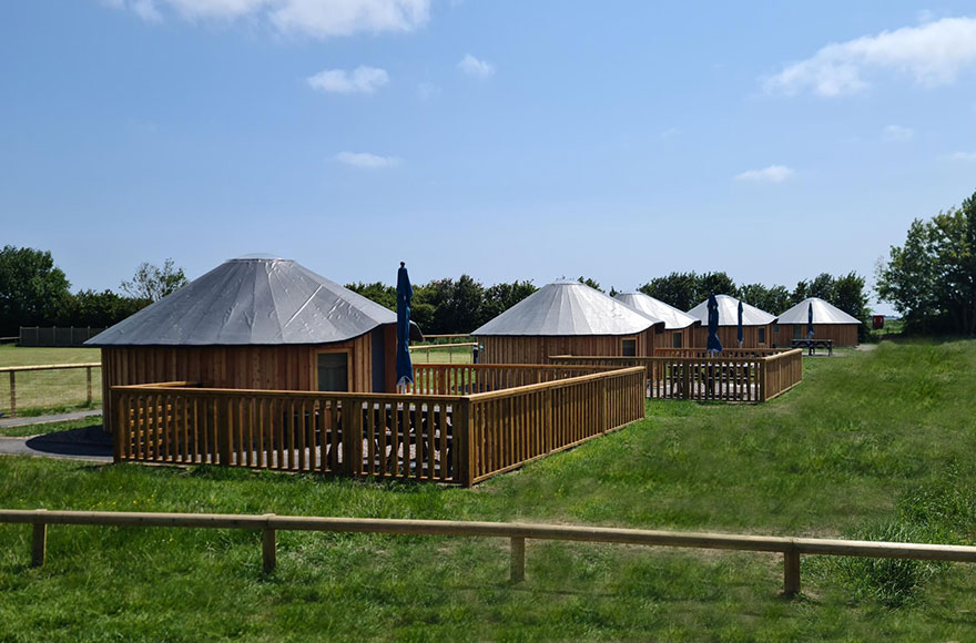 Several wooden yurts in a field, under a clear blue sky