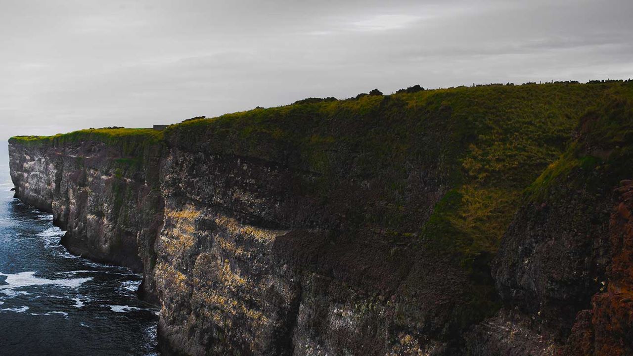 dark grassy cliffs surrounded by a blue sea