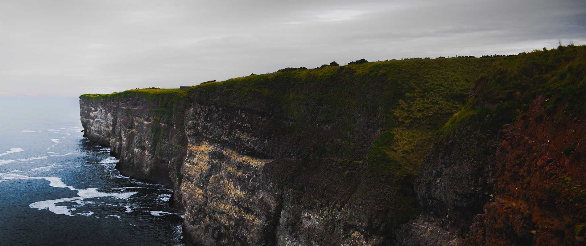 dark grassy cliffs surrounded by a blue sea