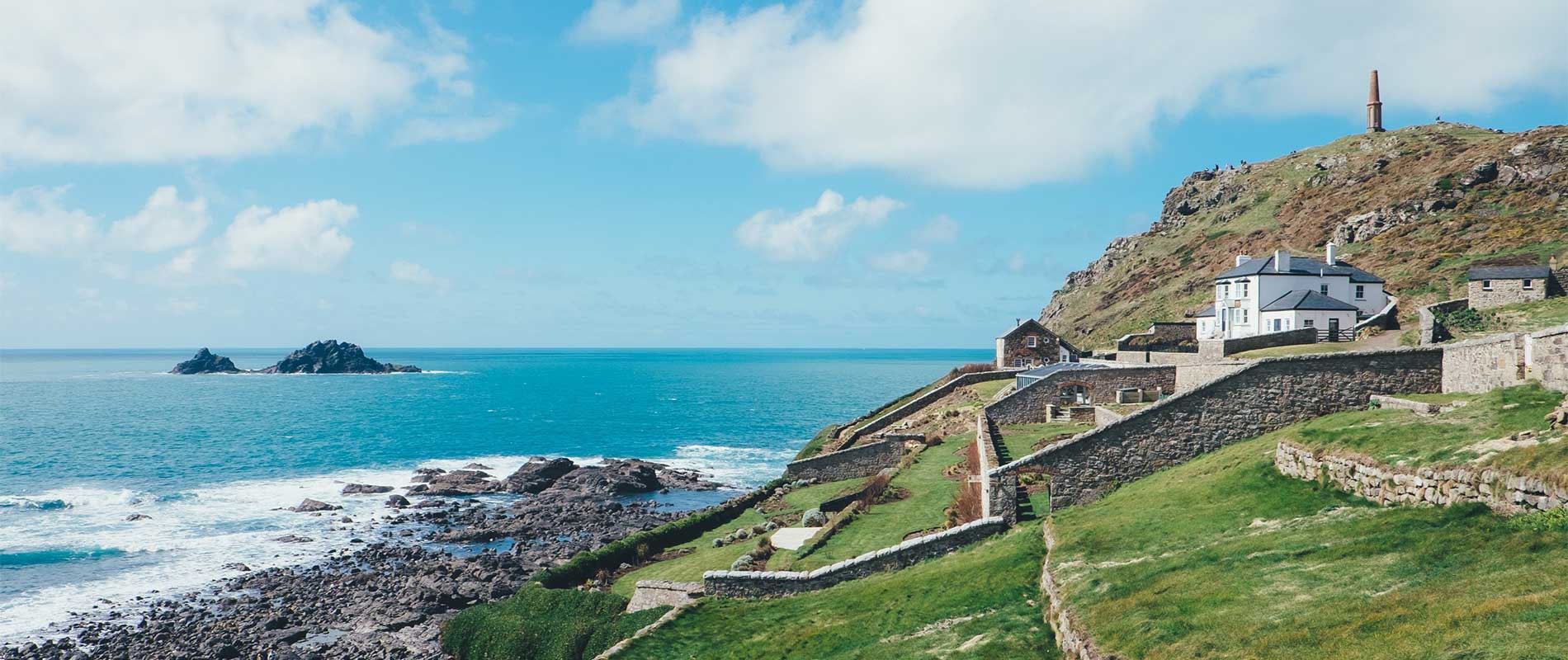 small headland of Cape Cornwall with houses fenced by stone walls overlooking the bright, blue sea