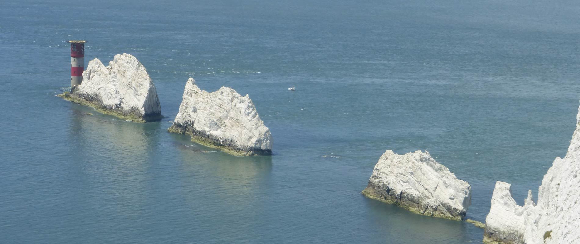 isle of wight white rocks protruding from the sea with a red and white lighthouse surrounded by a calm blue sea