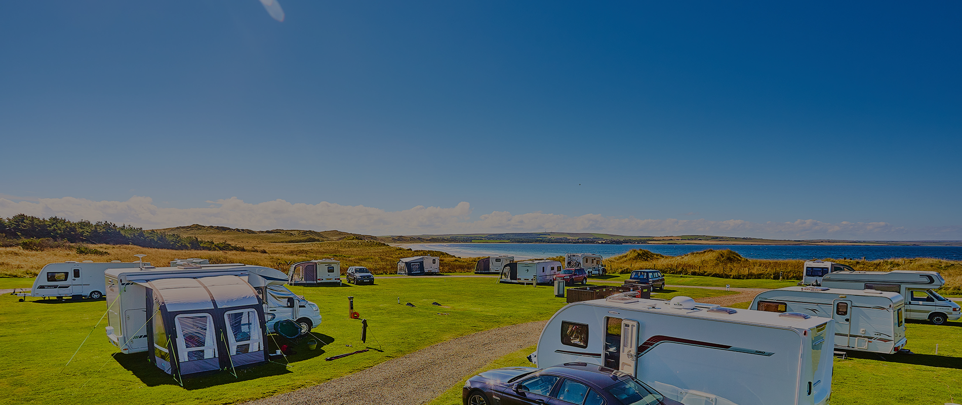 Caravans and motorhome paked on sunny Dunnet Bay over looking the clear sea