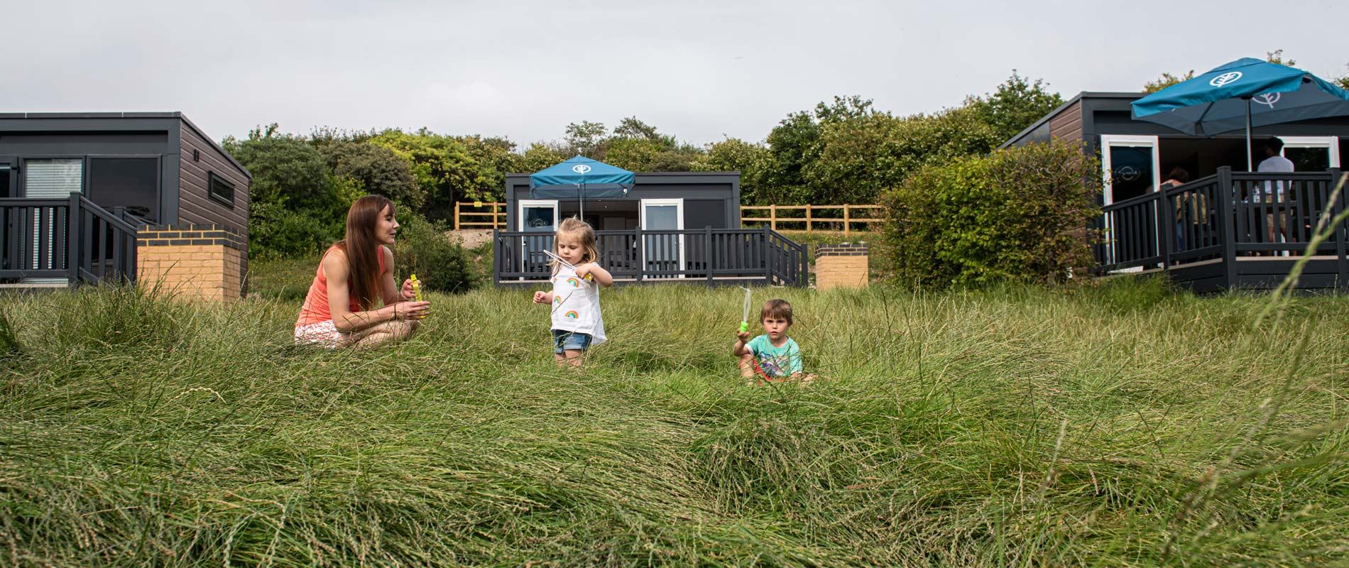 woman playing with her children int eh grass outside a glamping pod
