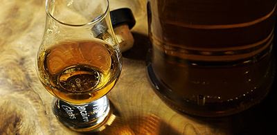 A glass of whiskey next to a whiskey barrel