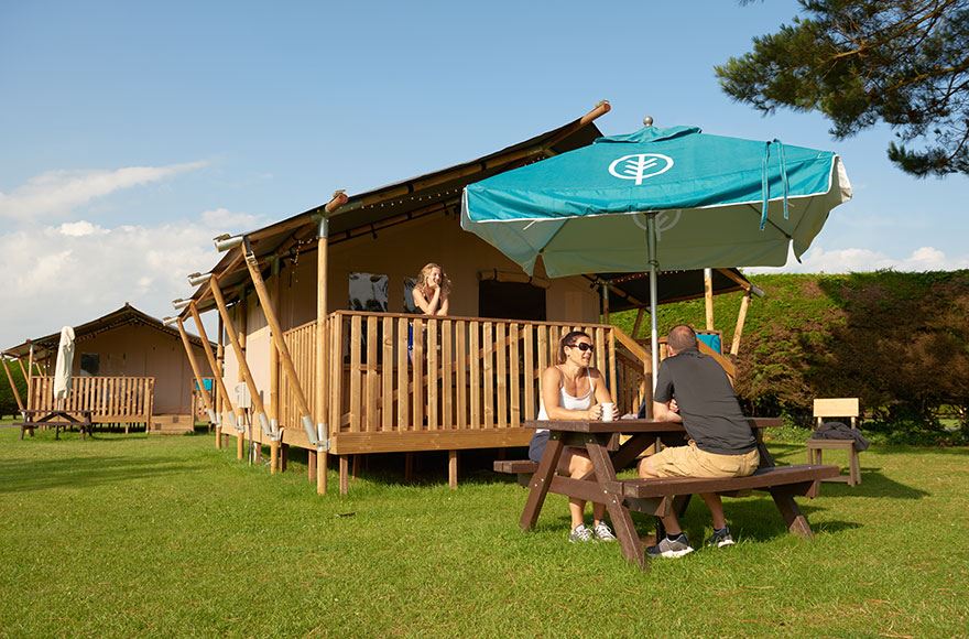 A couple relaxes at a picnic table in front of their  safari tent, enjoying each other's company in a tranquil outdoor setting