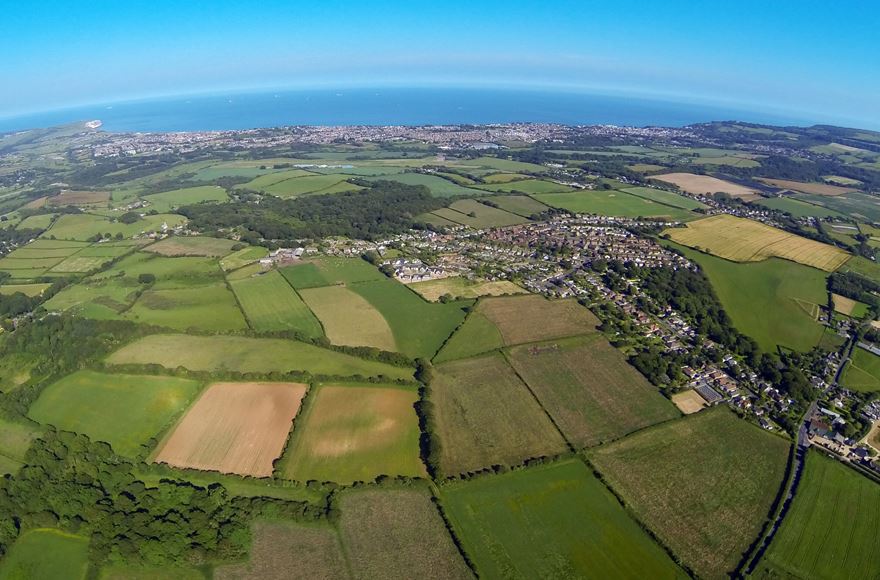 Aerial view showcasing a rural landscape with expansive fields bordered by a serene sea in the background