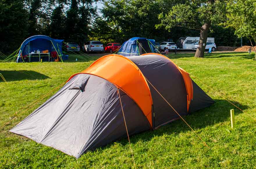 Orange and grey tent pitched up on the grass with other tents in the background