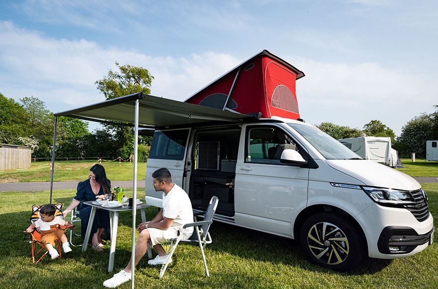 family sitting outside their campervan enjoying a meal in the sun