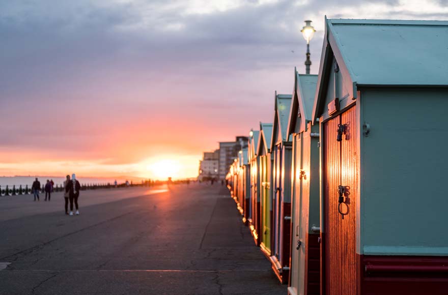 Line of beach huts with sun setting along Brighton promenade