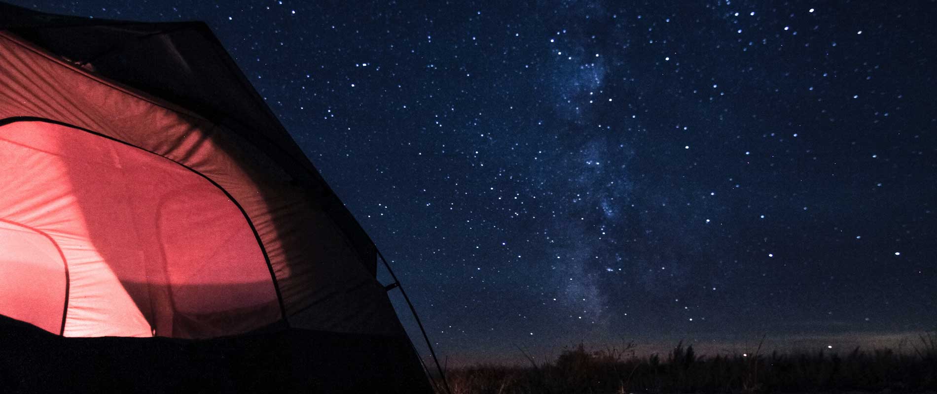 Red tent in a field at nighttime with clear, star-filled skies
