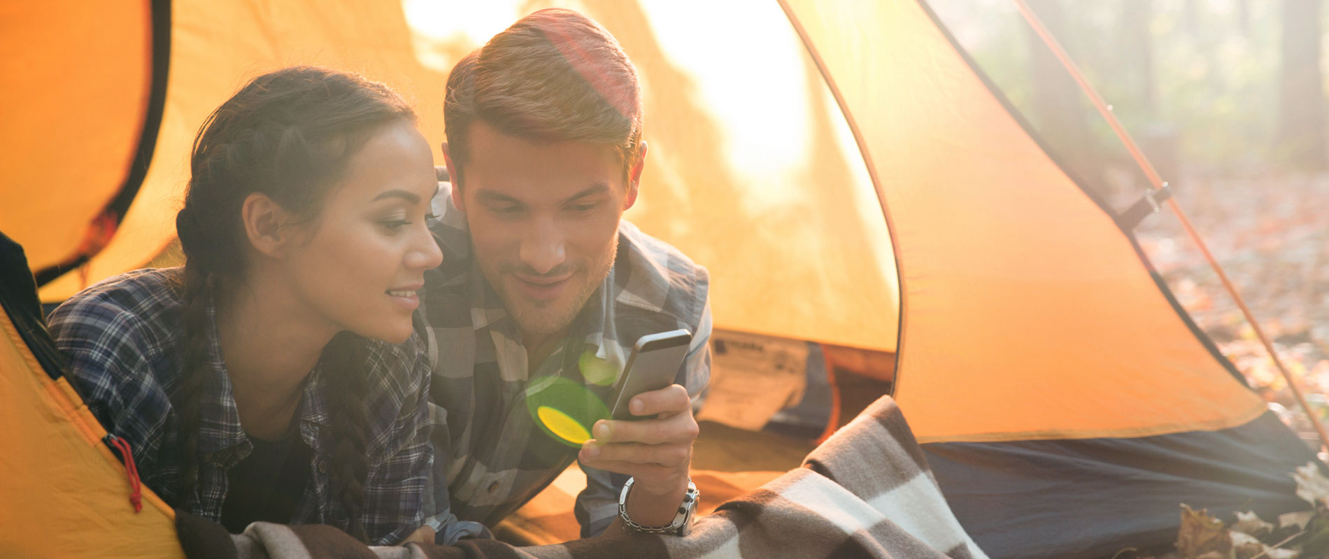 Couple using a mobile phone in their sun-filled tent