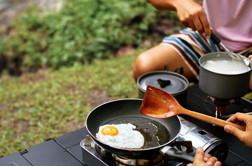 Frying eggs on a camping stove in green open space