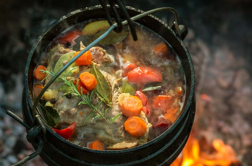 Vegetable and meat stew with carrots and rosemary in iron pot stewing over a campfire
