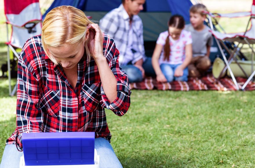 Mother rummaging through ice box as family sit by tent on picnic blanket